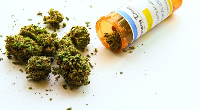 A prescription bottle tipped over with dried cannabis buds spilling out onto a surface.