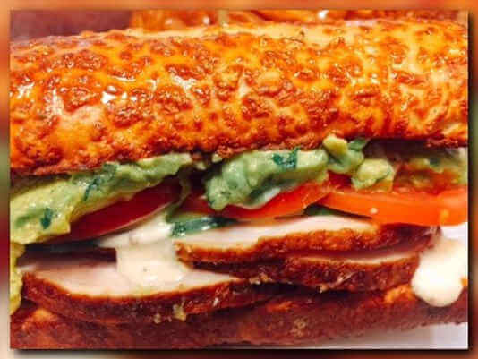 A sandwich with chicken, tomatoes and avocado on a white plate.