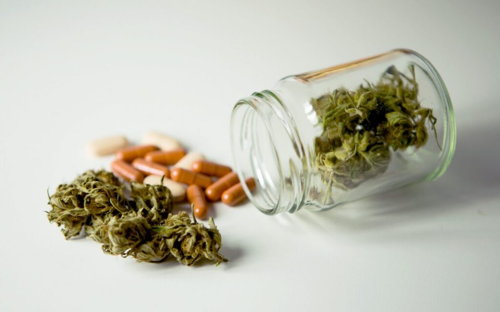 A glass jar filled with cannabis leaves and pills.