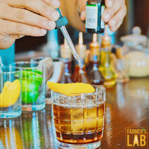  A person adding drops from a dropper bottle into a glass, it might be a CBD or cannabis-related tincture.